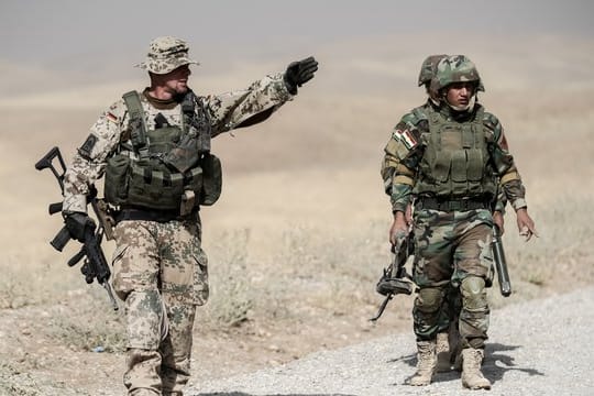 Bundeswehrsoldaten und kurdische Peshmerga Soldaten gehen in der Ausbildungseinrichtung Bnaslawa bei einer Übung am Rand einer Straße entlang.
