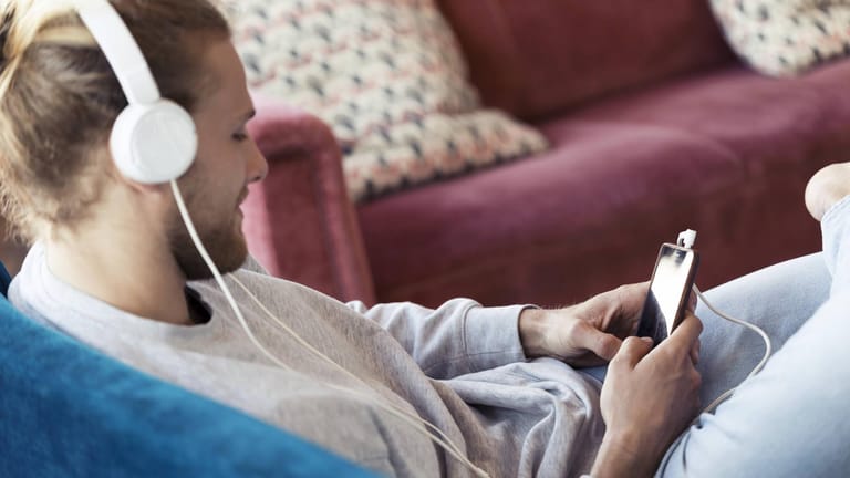 Ein Mann sitzt auf einem Sofa und hört Musik: In Hagen können Kunden der Stadtteilbibliothek nun kostenlos Musik streamen (Symbolbild).