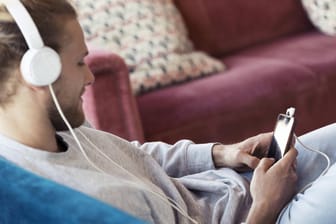 Ein Mann sitzt auf einem Sofa und hört Musik: In Hagen können Kunden der Stadtteilbibliothek nun kostenlos Musik streamen (Symbolbild).