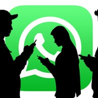 Umrisse von Menschen mit Smartphones in den Händen sind vor dem WhatsApp-Logo zu sehen: Wegen eines Rechtsstreits muss WhatsApp eine bestimmte Funktion in Deutschland abschalten.
