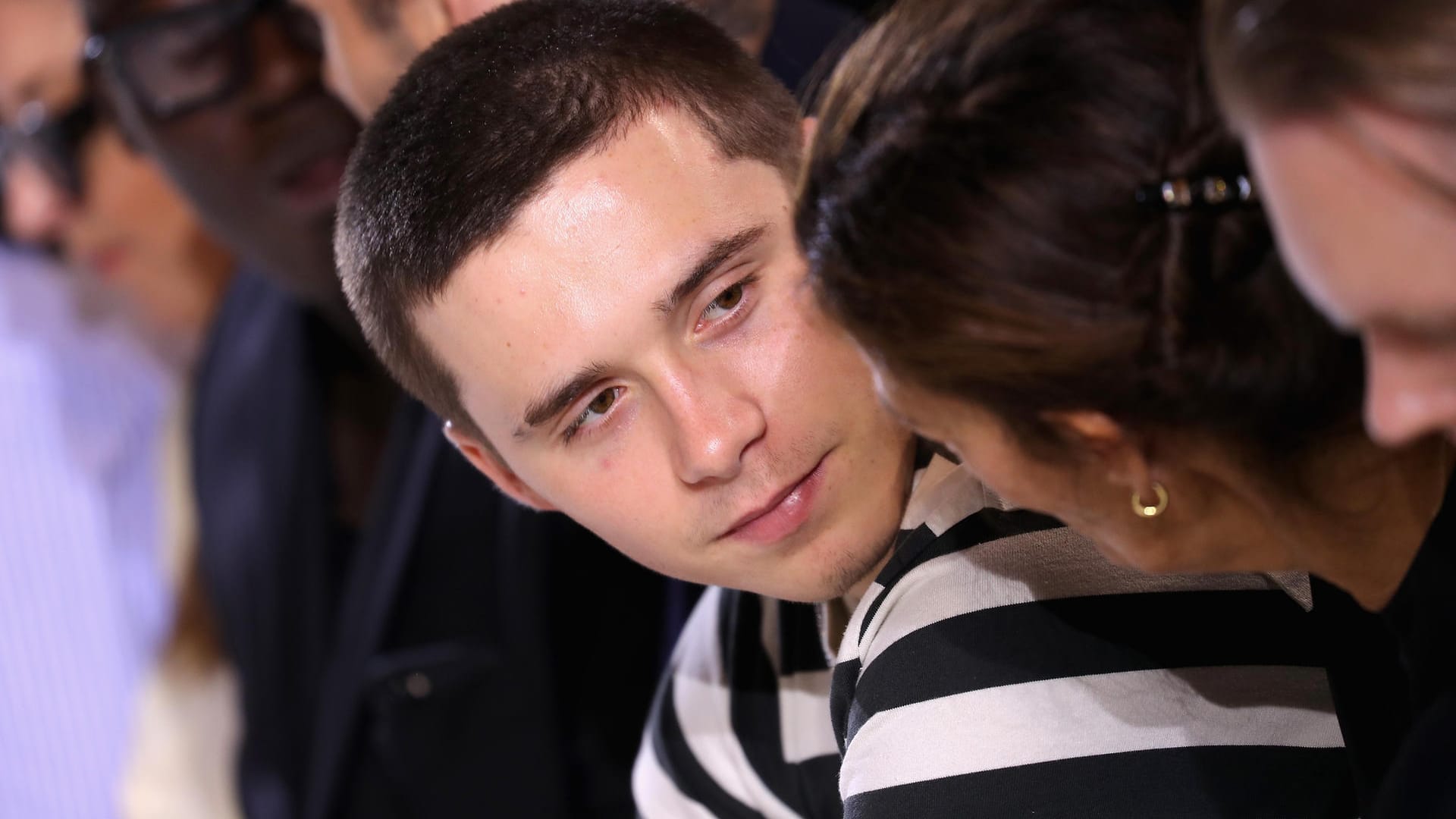 Brooklyn Beckham schaut eine Frau an, die den Kopf zu ihm geneigt hat.