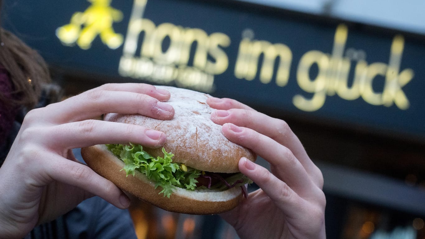 Hände halten einen Burger vor Eingang der Burgerkette "Hans im Glück"