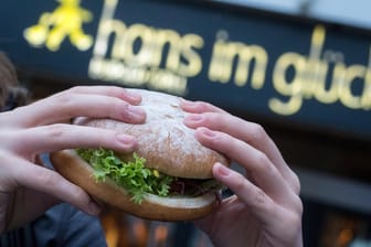 Hände halten einen Burger vor Eingang der Burgerkette "Hans im Glück"