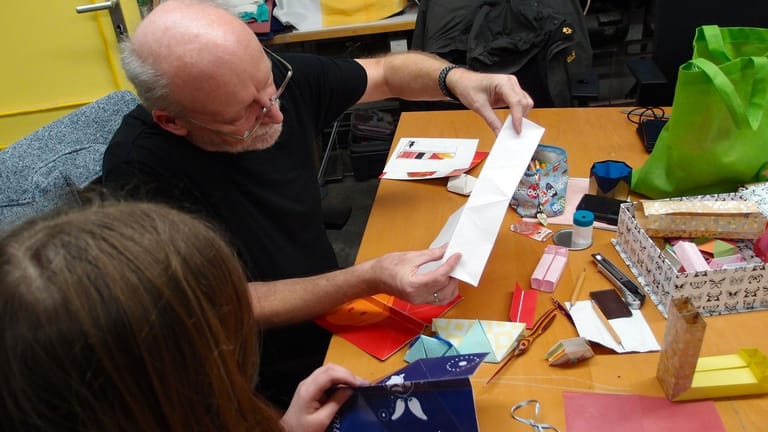 In der Origami-Ecke zeigt Hans-Werner (67) der elfjährigen „Charlie“, wie man das Papier richtig faltet.