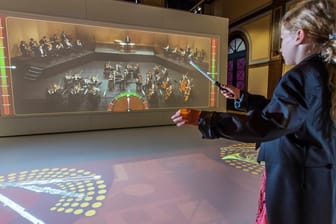 Ein Kind steht vor einem virtuellen Orchester: Im Toccarion können Kinder selbst die Welt der Musik entdecken.