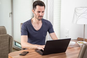 Mann am Laptop: Über Online-Kleinanzeigen lässt sich, bequem am Computer, von zu Hause aus einkaufen und verkaufen. Vorsicht jedoch vor trickreichen Betrügern.