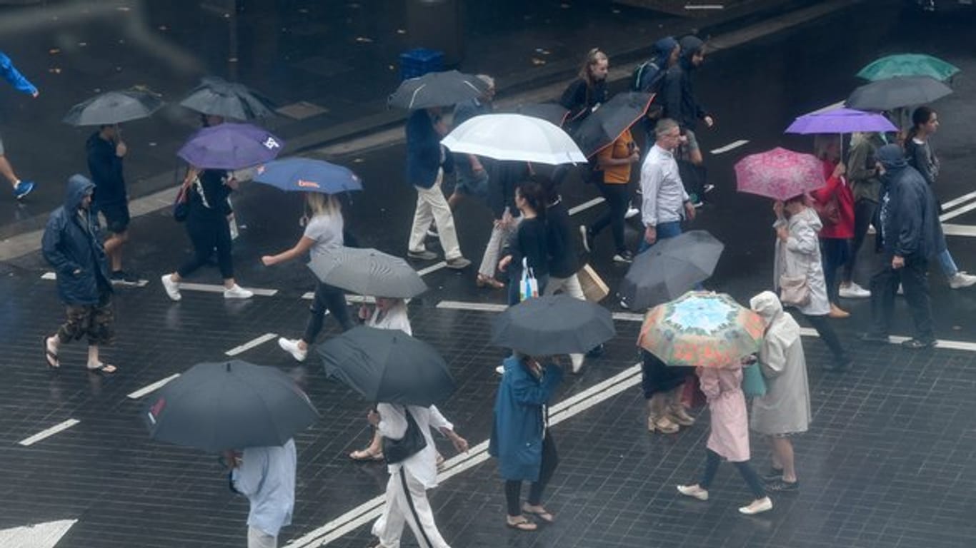 Fußgänger schützen sich mit Regenschirmen vor starkem Regen.