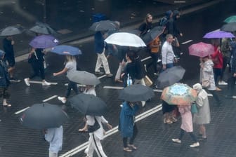 Fußgänger schützen sich mit Regenschirmen vor starkem Regen.