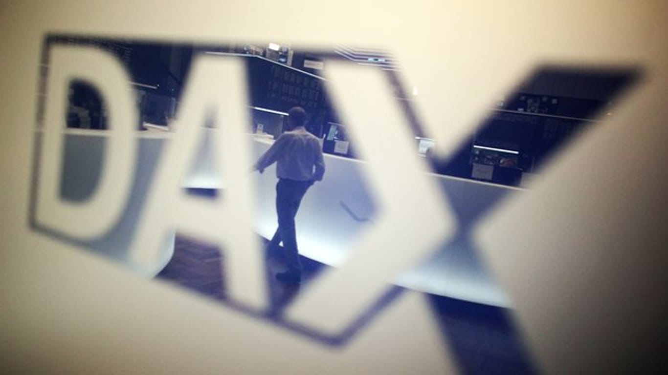 Ein Händler geht über das Parkett in der Börse in Frankfurt am Main und spiegelt sich dabei in einem Logo des Deutschen Aktienindexes (DAX).