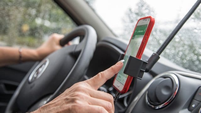 Innenraum eines Autos. Eine Frau bedient ein Smartphone: Wird die Navi-App im Auto genutzt, sollte das Smartphone lieber in einer passenden Halterung stecken.