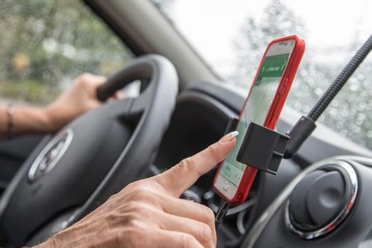 Innenraum eines Autos. Eine Frau bedient ein Smartphone: Wird die Navi-App im Auto genutzt, sollte das Smartphone lieber in einer passenden Halterung stecken.