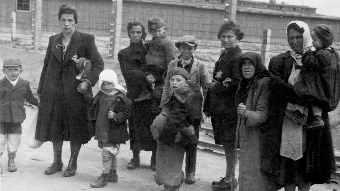 Jüdische Mütter und Kinder im KZ Auschwitz gehen am elektrischen Zaun vorbei in Richtung Gaskammer.