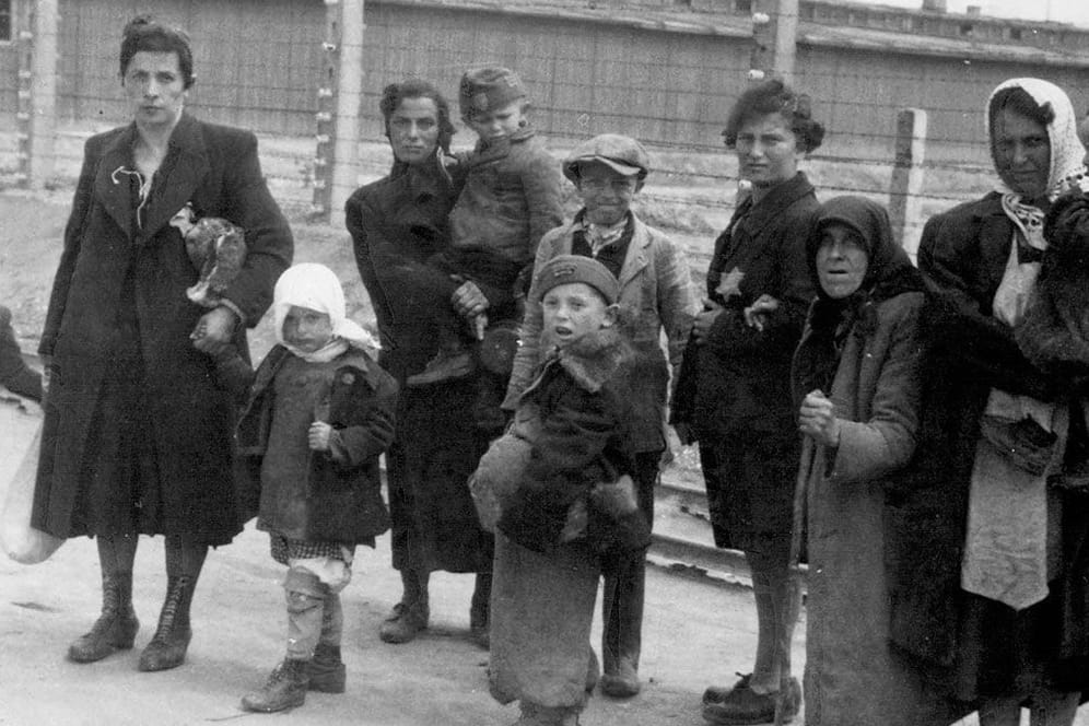 Jüdische Mütter und Kinder im KZ Auschwitz gehen am elektrischen Zaun vorbei in Richtung Gaskammer.