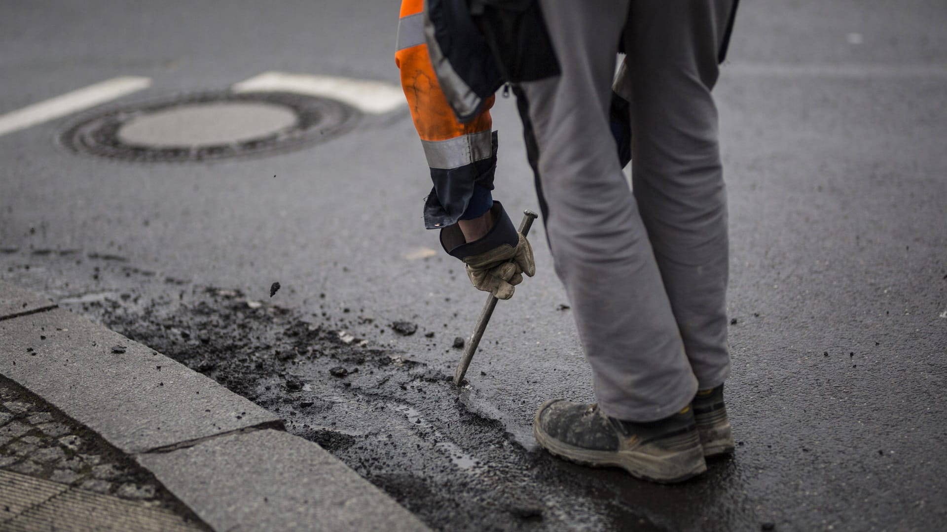 Ein Mann bearbeitet einen Straße mit Hammer und Meißel: In Wolfsburg sind Arbeiter des Tiefbauamtes wegen eines Rohrbruches im Einsatz.