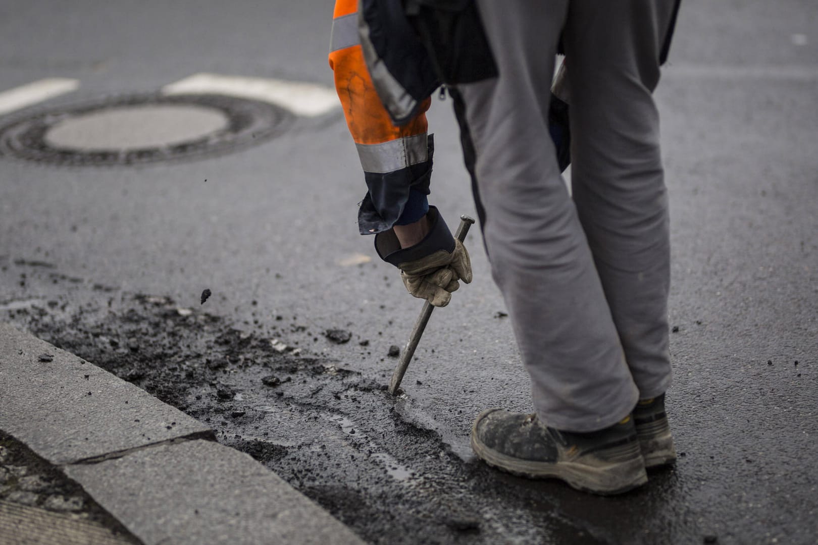 Ein Mann bearbeitet einen Straße mit Hammer und Meißel: In Wolfsburg sind Arbeiter des Tiefbauamtes wegen eines Rohrbruches im Einsatz.