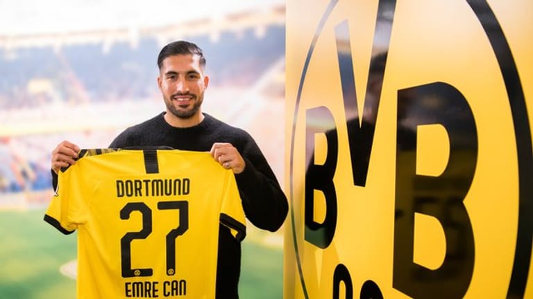Emre Can posiert neben dem Logo von Borussia Dortmund mit einem Trikot des Vereins.