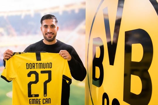 Emre Can posiert neben dem Logo von Borussia Dortmund mit einem Trikot des Vereins.