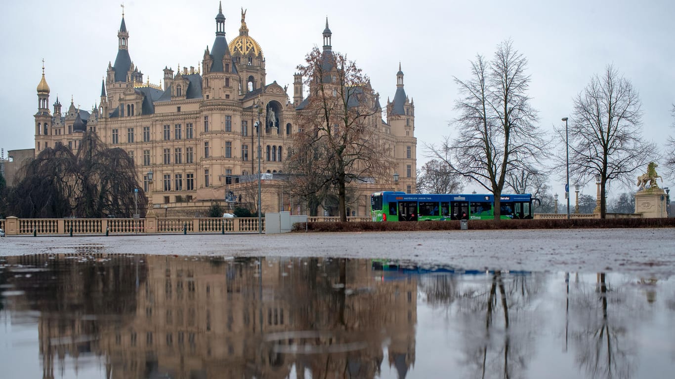 Das Schweriner Schloss spiegelt sich in einer Regenpfütze: Nicht nur Norddeutschland muss sich auf viele Regenschauer einstellen.