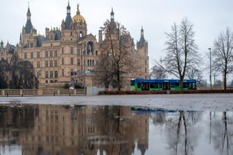 Das Schweriner Schloss spiegelt sich in einer Regenpfütze: Nicht nur Norddeutschland muss sich auf viele Regenschauer einstellen.