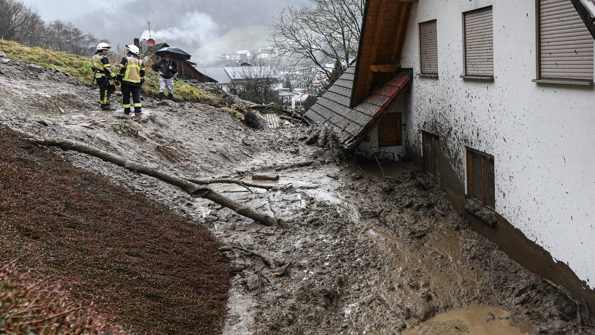 Simonswald in Baden-Württemberg: Feuerwehrmänner stehen vor an einem Haus, das von einer Schlammlawine getroffen wurde. Simonswald in Baden-Württemberg: Feuerwehrmänner stehen vor an einem Haus, das von einer Schlammlawine getroffen wurde.