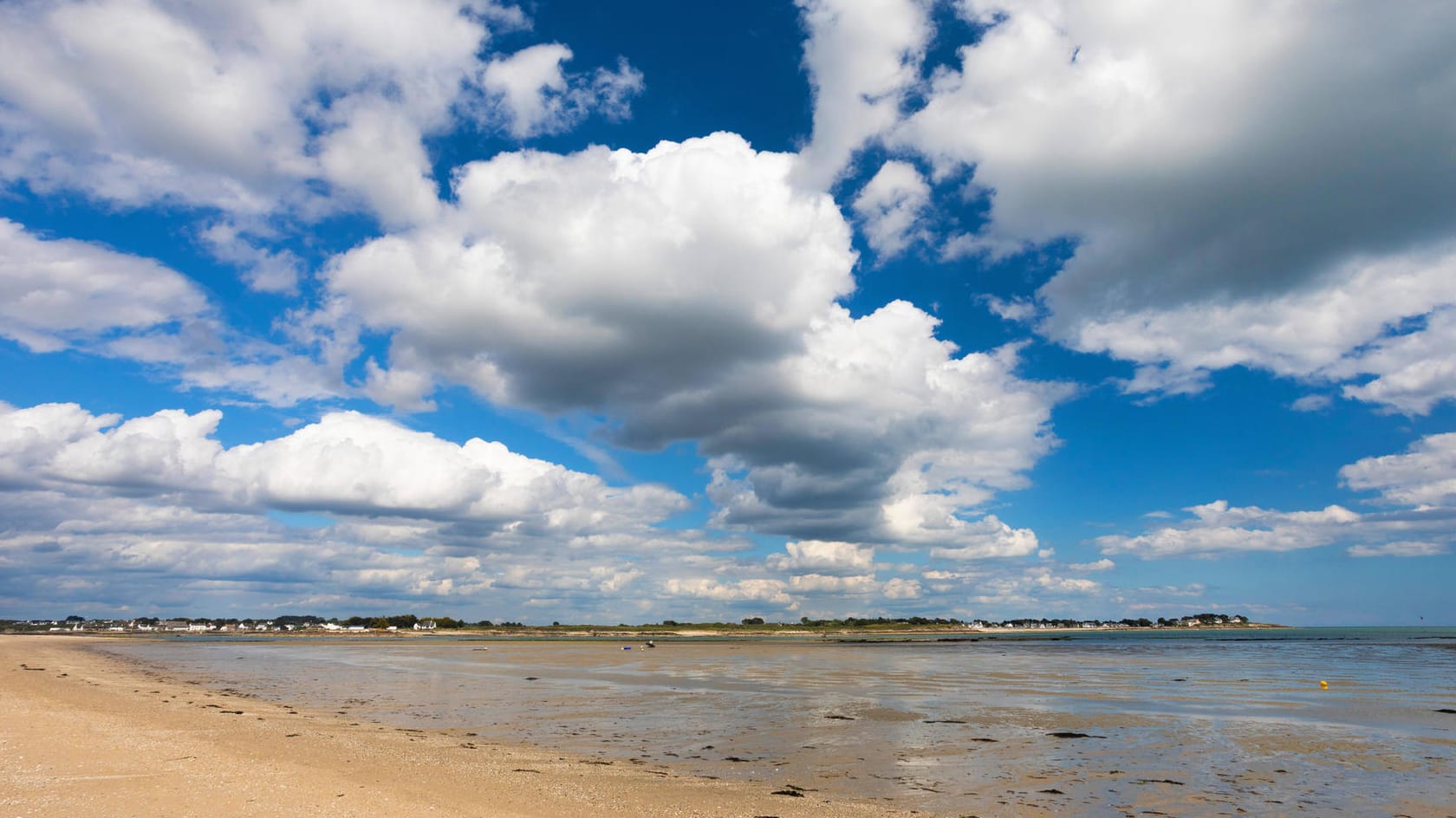 Quellwolken ziehen über einen Strand: Cumuluswolken bilden sich nah an der Erdoberfläche, haben eine flache Unterseite und sind nach oben hin strahlend weiß und bauschig. Sie tragen zur Kühlung bei, da sie ankommende Sonnenstrahlen reflektieren.