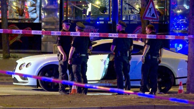 Polizisten stehen neben dem Auto des Rockerbosses auf dem Millerntorplatz an der Reeperbahn, nachdem die Schüsse gefallen waren. Polizisten stehen neben dem Auto des Rockerbosses auf dem Millerntorplatz an der Reeperbahn, nachdem die Schüsse gefallen waren.