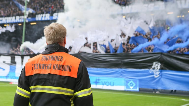 Ein Feuerwehrmann schaut auf die Kurve des HSV: Die Pyro-Premiere des Hamburger SV im Spiel gegen den KSC ist geglückt.