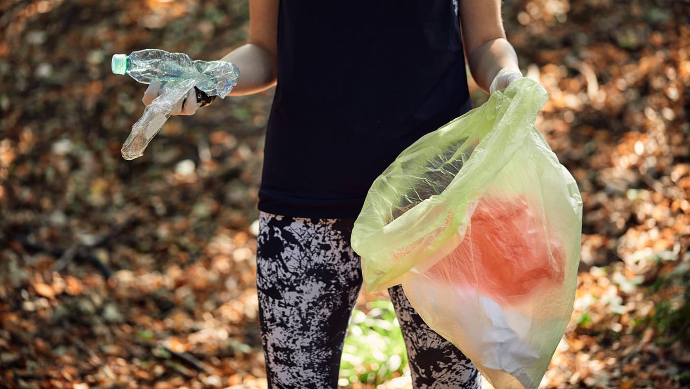 Eine Frau sammelt Plastikmüll im Wald ein: In Bielefeld will ein Aktionsprojekt die Stadt sauberer machen (Symbolbild).