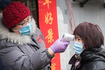 Eine Gemeindemitarbeiterin misst mit einem Fieberthermometer die Körpertemperatur einer Passantin in einer Straße in Wuhan.
