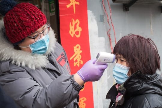 Eine Gemeindemitarbeiterin misst mit einem Fieberthermometer die Körpertemperatur einer Passantin in einer Straße in Wuhan.