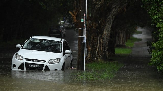 Ein Auto steht in einer überfluteten Straße in Sydney. Ein Auto steht in einer überfluteten Straße in Sydney.