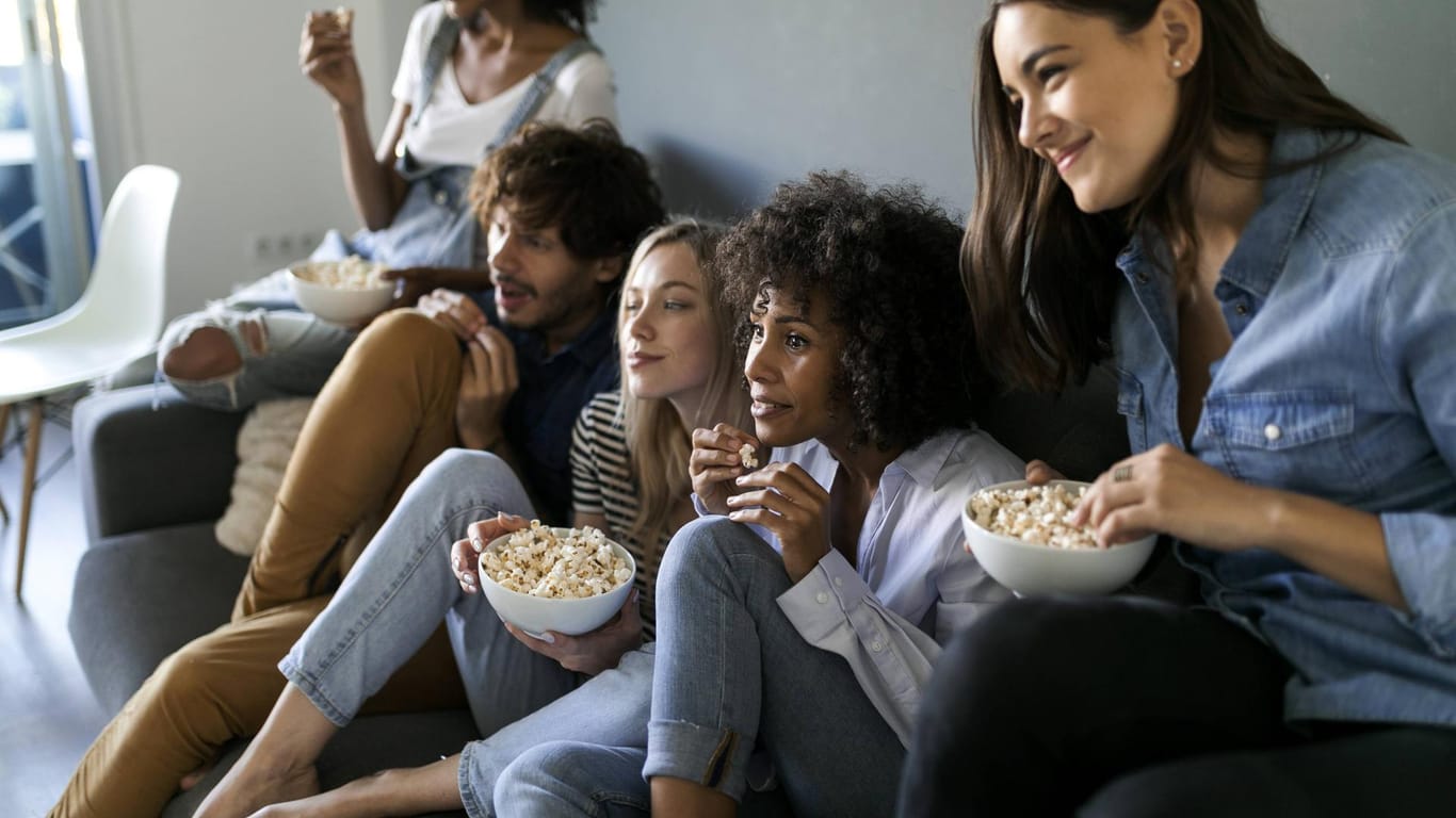Menschen sitzen auf einem Sofa und essen Popcorn: Zu Amazon Prime Video und Netflix gibt es auch kostenlose Alternativen.
