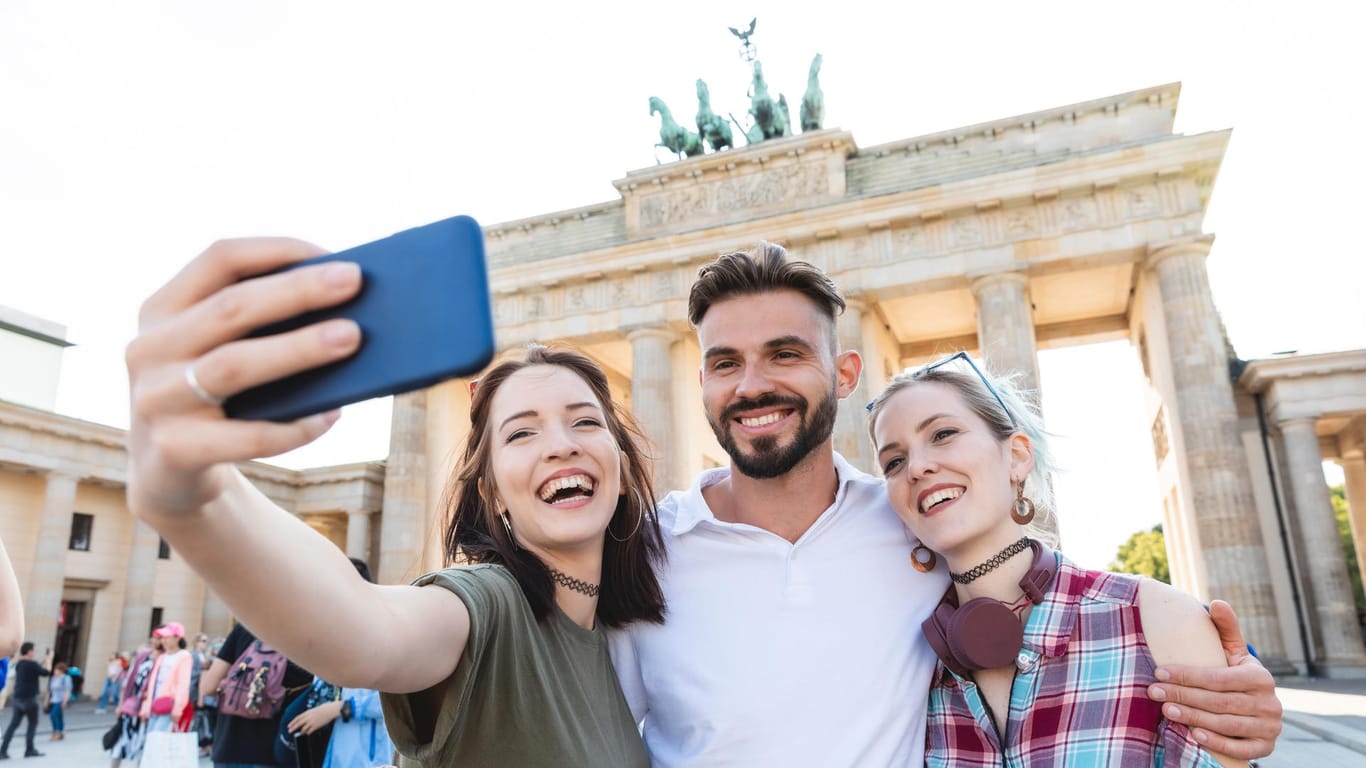 Vor dem Brandenburger Tor in Berlin: Selfie-Portrait dreier junger Menschen.