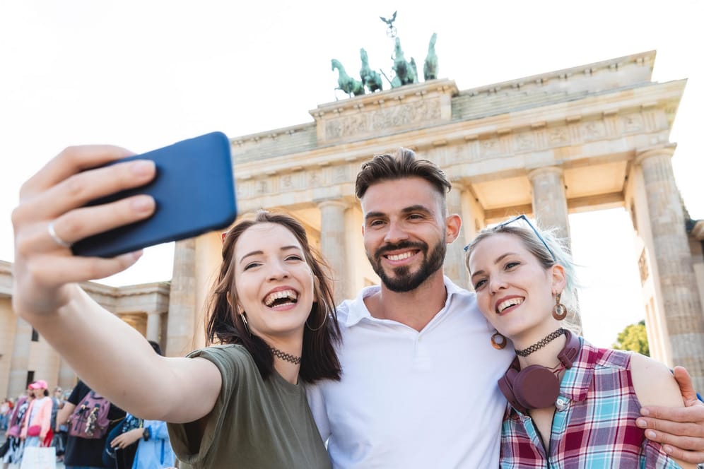 Vor dem Brandenburger Tor in Berlin: Selfie-Portrait dreier junger Menschen.