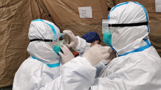 Ärzte richten sich in einem umgebauten Krankenhaus in Wuhan ihre Schutzbrillen. Ärzte richten sich in einem umgebauten Krankenhaus in Wuhan ihre Schutzbrillen.