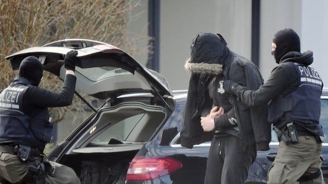 Eine Person wird von einem maskierten Polizisten in den Bundesgerichtshof in Karlsruhe gebracht.