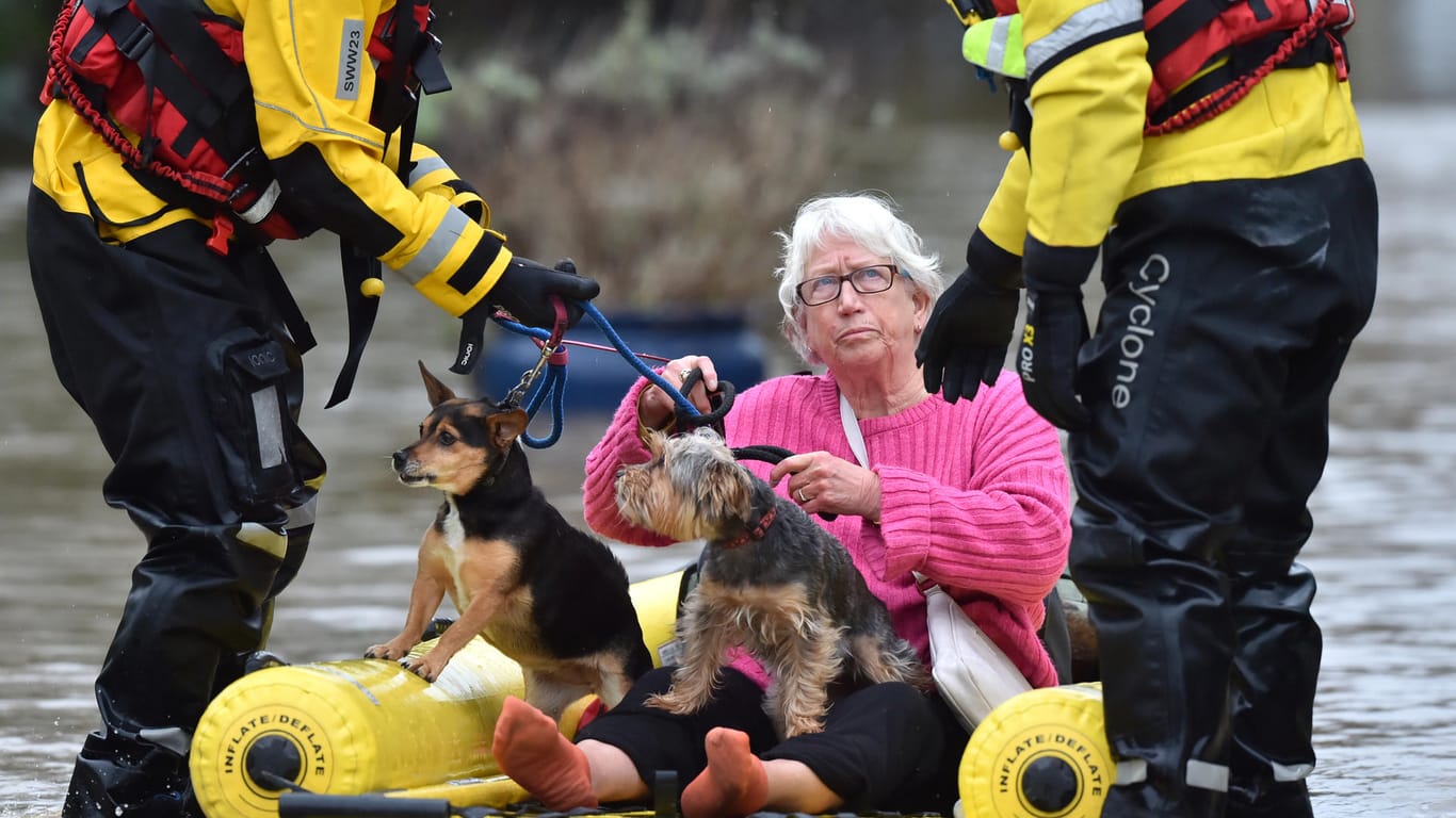 Rettungskräfte bringen eine Frau und ihre zwei Hunde per Schlauchboot in Sicherheit: In England sorgt Sturm "Dennis" für Chaos.