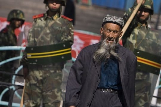 Ein Angehöriger der uigurischen Minderheit in der Unruheregion Xinjiang geht an chinesischen Sicherheitskräften vorbei.