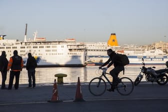 Passanten stehen vor den angedockten Fähren im Hafen von Piräus.