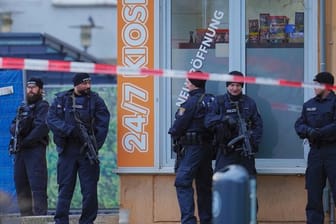 Mit Maschinenpistolen bewaffnete Einsatzkräfte der Polizei vor einem Kiosk am Tatort in Hanau-Kesselstadt.