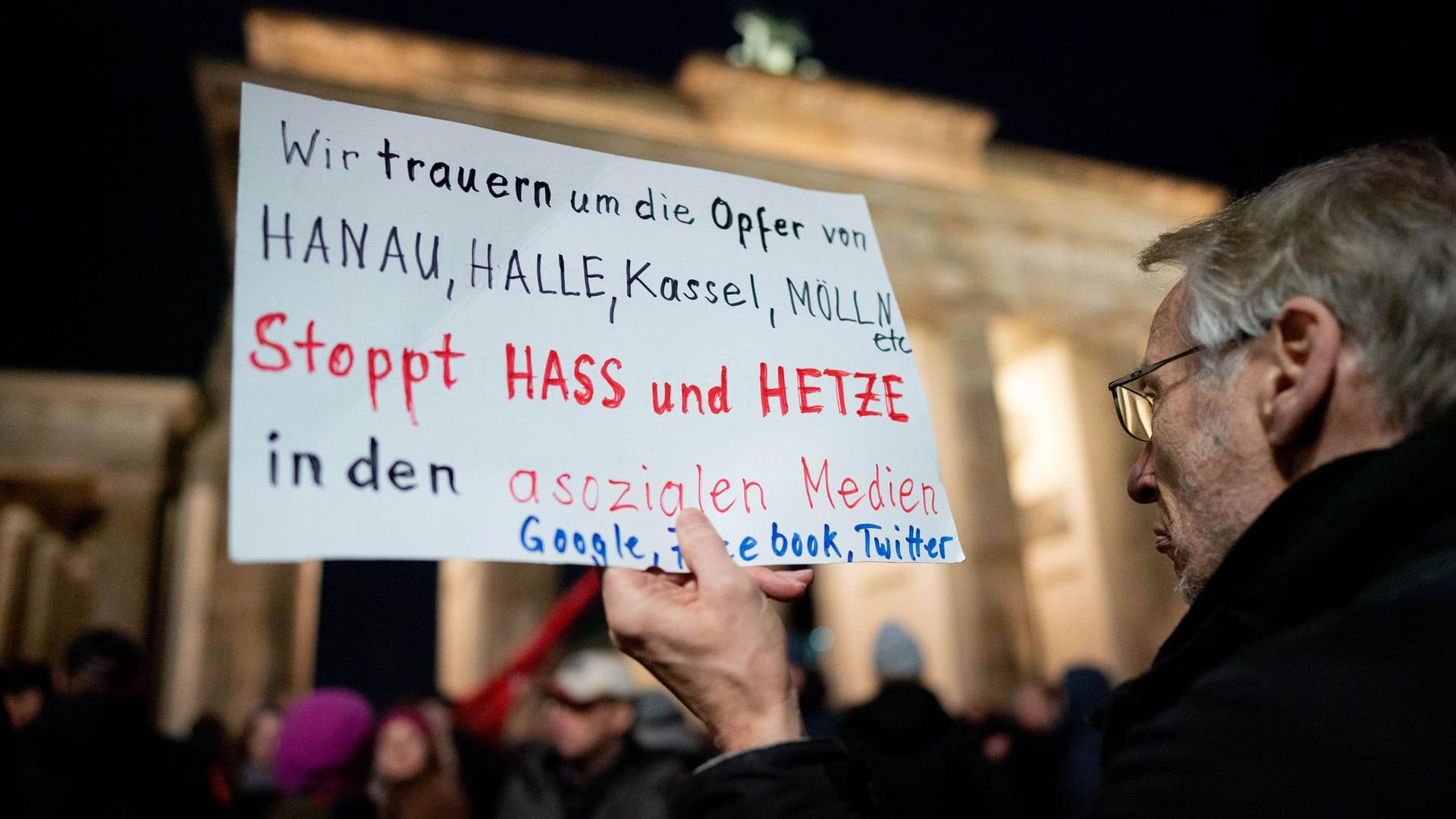 Ein Mann hält ein Plakat hoch: Menschen kamen zur Mahnwache am Brandenburger Tor zusammen.