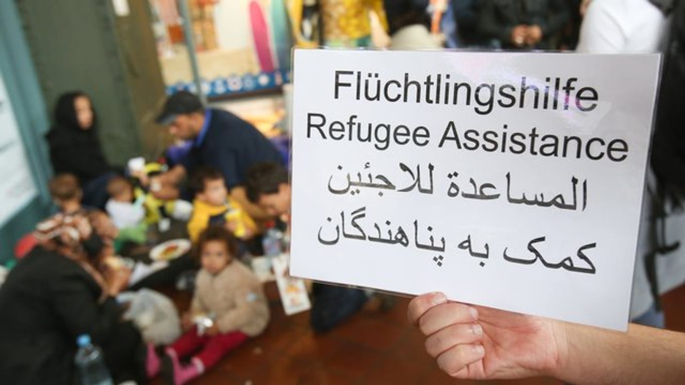 Ein freiwilliger Helfer hält 2015 im Hauptbahnhof in Hamburg ein Schild auf deutsch, englisch und arabisch, auf der Hilfe für Flüchtlinge angeboten wird.