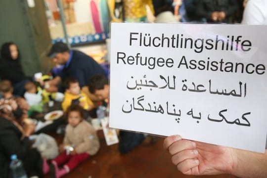 Ein freiwilliger Helfer hält 2015 im Hauptbahnhof in Hamburg ein Schild auf deutsch, englisch und arabisch, auf der Hilfe für Flüchtlinge angeboten wird.