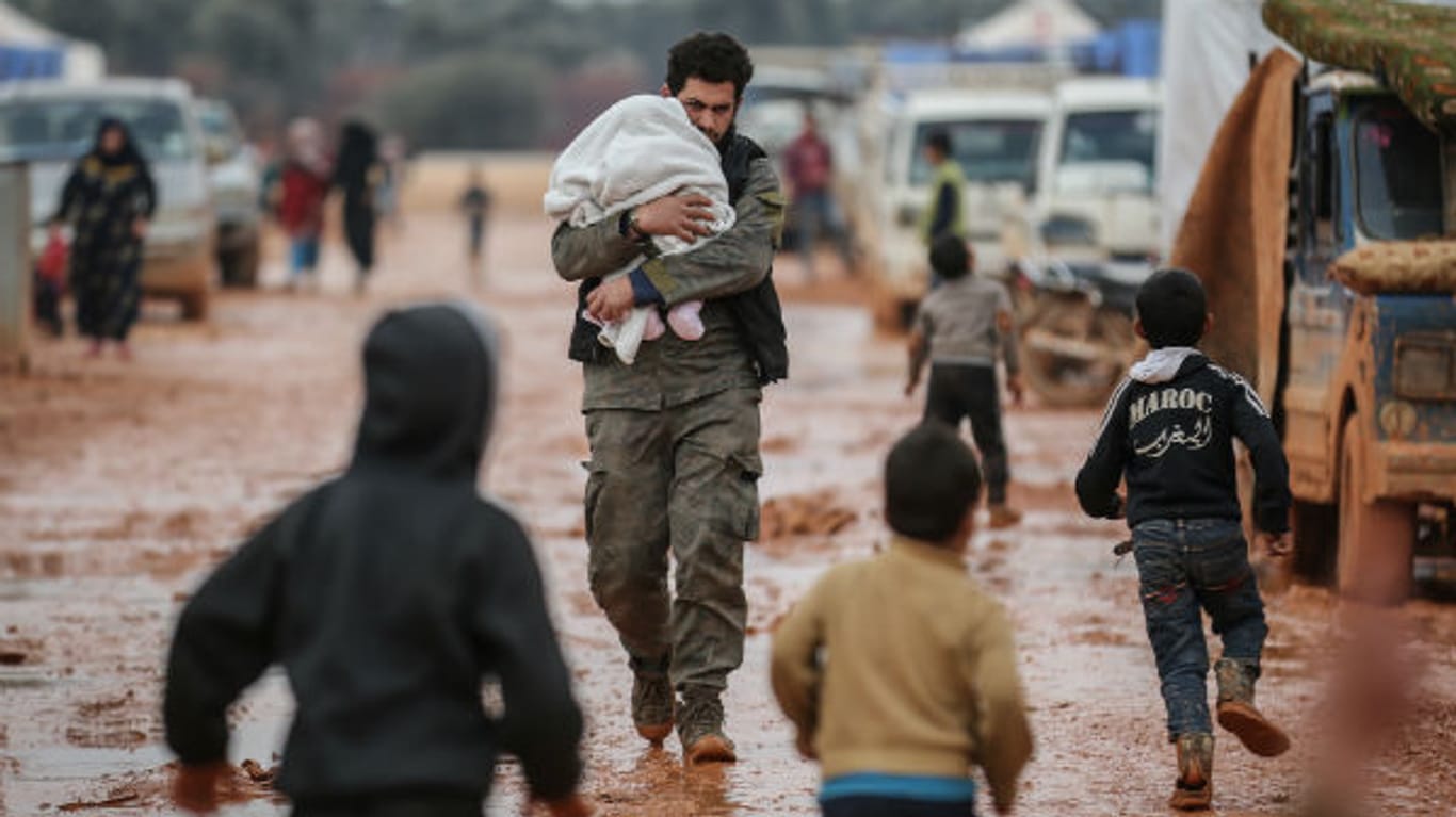 Ein Mann trägt sein Baby durch den Matsch: Die Zustände in den Behelfslagern sind fatal.