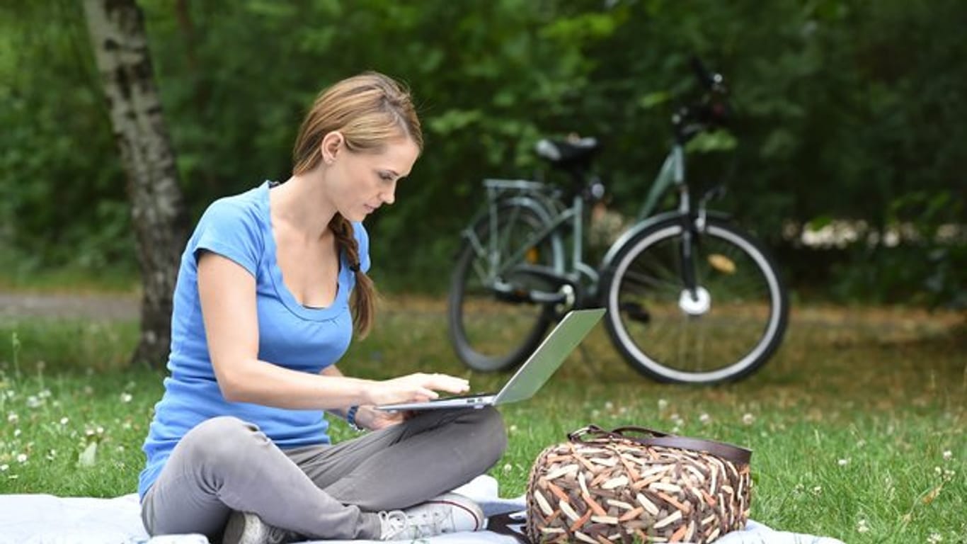 Frau sitzt im Park an einem Laptop: Über VPN-Verbindungen lässt sich auch im öffentlichen W-LAN sicher surfen.