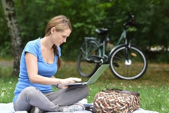Frau sitzt im Park an einem Laptop: Über VPN-Verbindungen lässt sich auch im öffentlichen W-LAN sicher surfen.