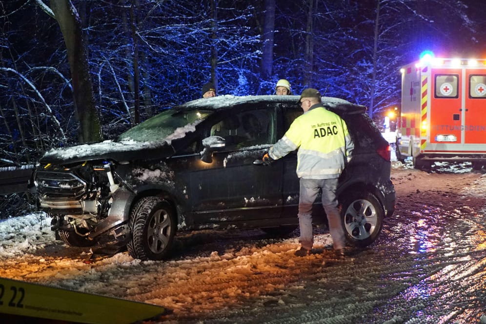 Bayern: Nach einem Unfall auf einer schneebedeckten Straße bei Burglengenfeld im Landkreis Schwandorf kümmern sich Helfer um ein Fahrzeug.