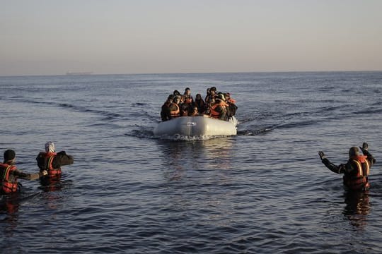 Freiwillige Helfer nehmen auf der griechischen Lesbos ein kaum seetüchtiges Gummiboot mit Flüchtlingen aus der Türkei in Empfang.