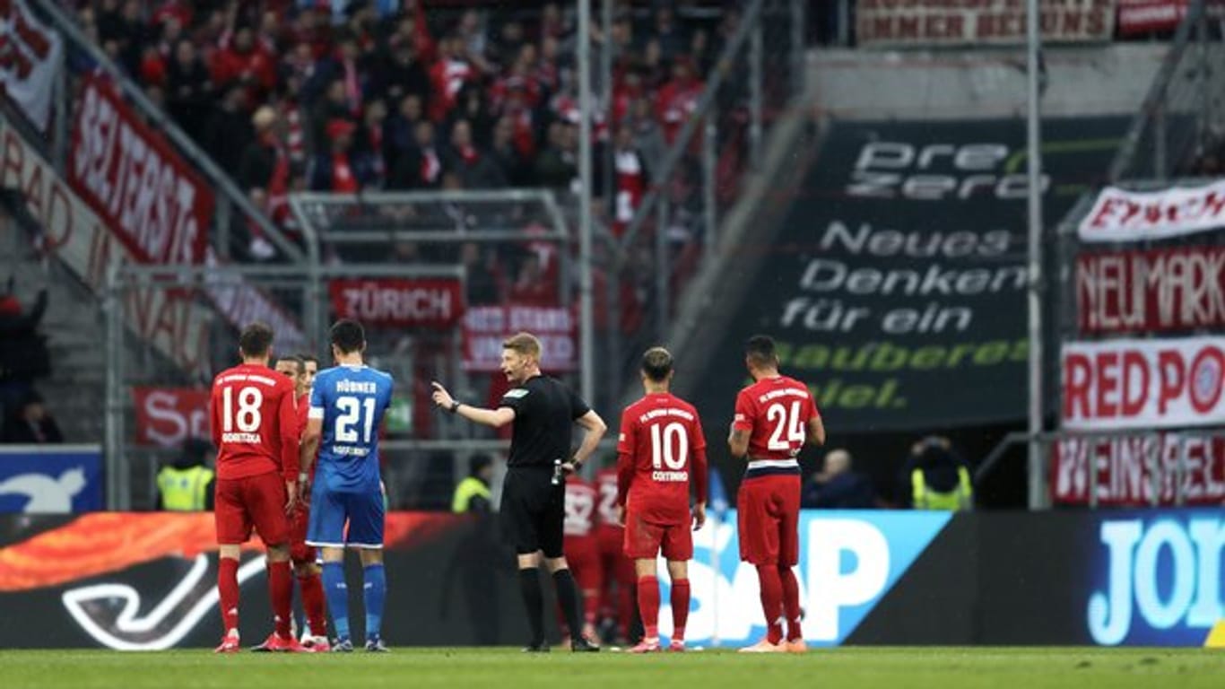 Schiedsrichter Christian Dingert (M) spricht mit Spielern, während Fans auf der Tribüne ein beleidigendes Banner zeigen.