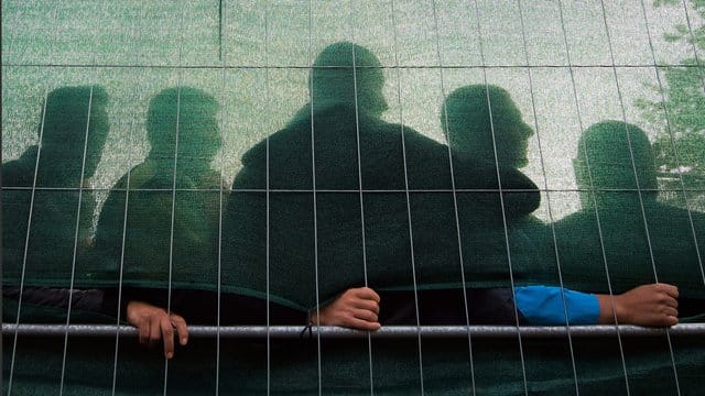 Flüchtlinge stehen im Spätsommer 2015 in einer Flüchtlingsunterkunft in Hamburg hinter einem Zaun. Flüchtlinge stehen im Spätsommer 2015 in einer Flüchtlingsunterkunft in Hamburg hinter einem Zaun.